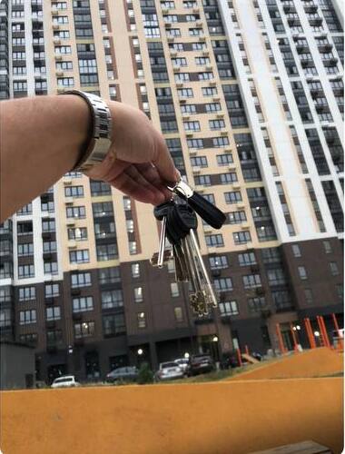 Ключи от новой квартиры на фоне новостройки — покупатель Евгений